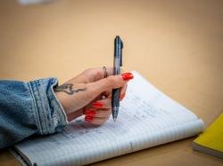 “这是一张特写照片，一只指甲红的手拿着笔做笔记."