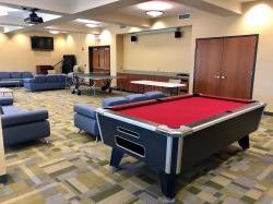 The common area in Sinatra Hall featuring some couches and chairs, a pool table and a television.